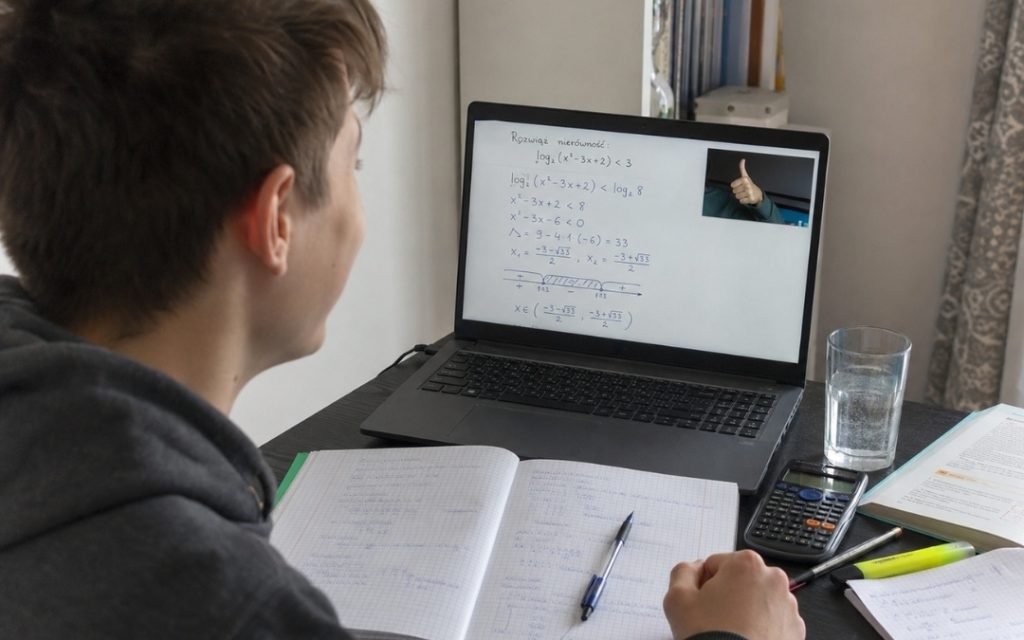 Nastolatek uśmiecha się do laptopa z rozwiązanym zadaniem i kciukiem w górę od korepetytora.
