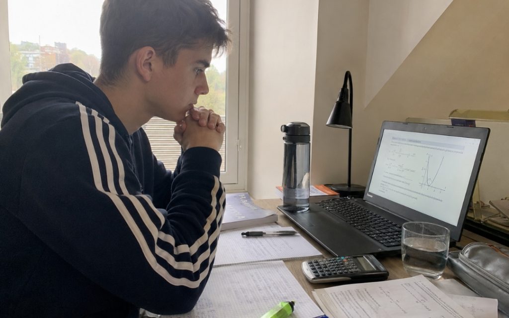 Skupiony maturzysta w sportowej bluzie patrzy w laptop z arkuszem maturalnym.