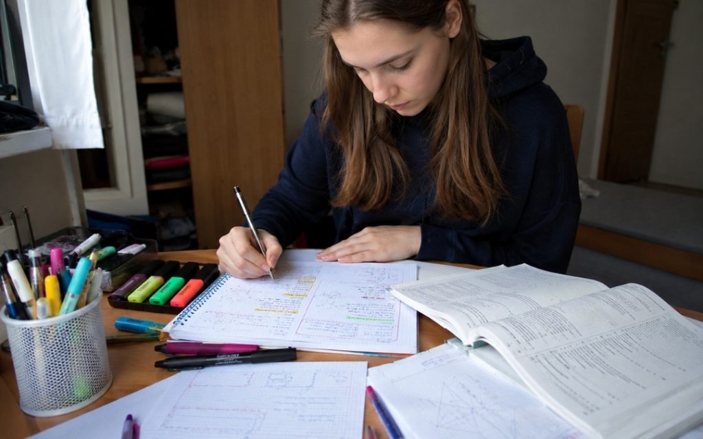 Nastolatka tworzy kolorowe notatki w zeszycie, korzystając z podręcznika, zakreślaczy i materiałów do matematyki.