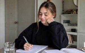 Uśmiechnięta nastolatka zapisuje notatki w zeszycie podczas spokojnej nauki przy biurku.
