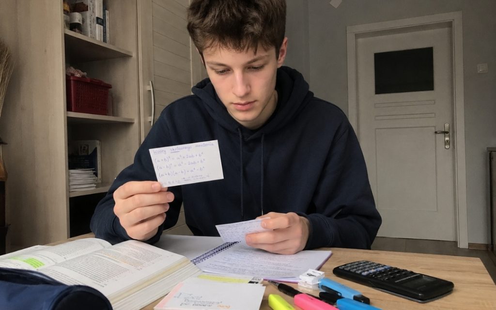 Nastolatek powtarza wzory matematyczne z fiszek, siedząc przy biurku z podręcznikiem i zakreślaczami.