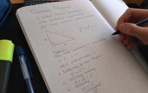 Zbliżenie na zeszyt z uproszczonym wyjaśnieniem twierdzenia Pitagorasa, rysunkiem trójkąta i obliczeniami.