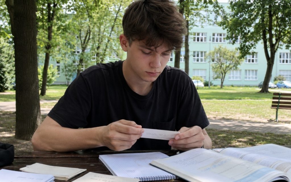 Licealista uczy się matematyki z fiszek w parku, siedząc przy stole z zeszytem i podręcznikiem.