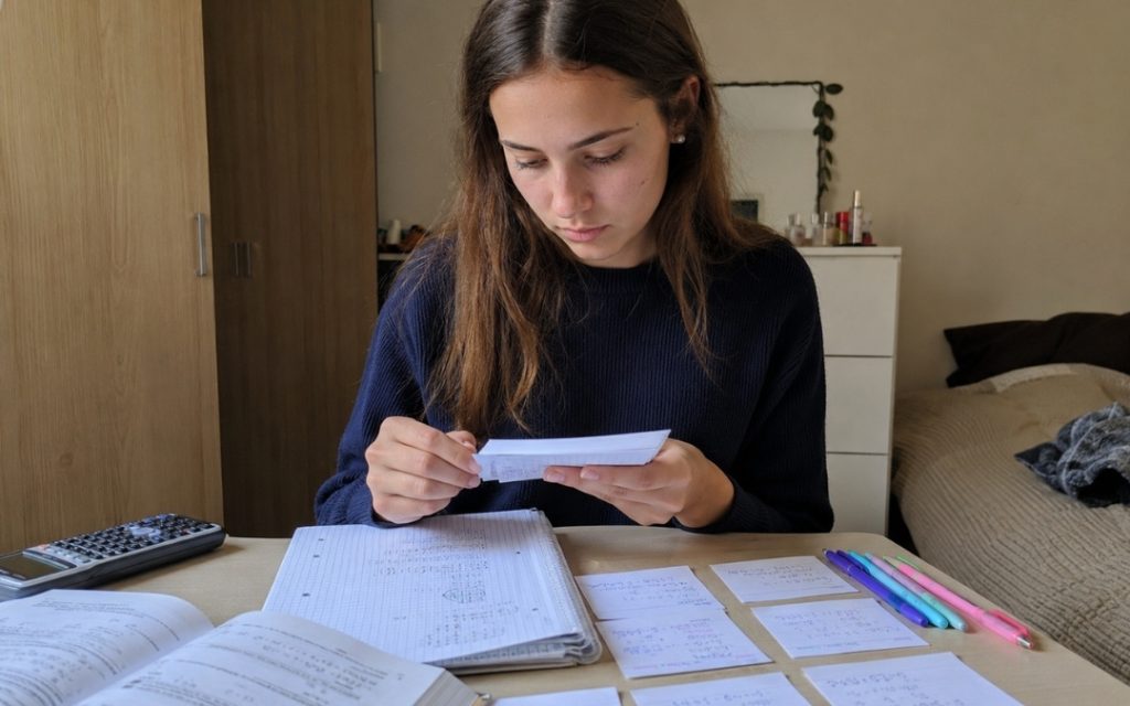 Licealistka uczy się matematyki z fiszek przy biurku, korzystając z zeszytu, podręcznika i kalkulatora.