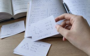 Zbliżenie na fiszkę matematyczną z rysunkiem trójkąta, wzorami trygonometrycznymi i notatkami w zeszycie.