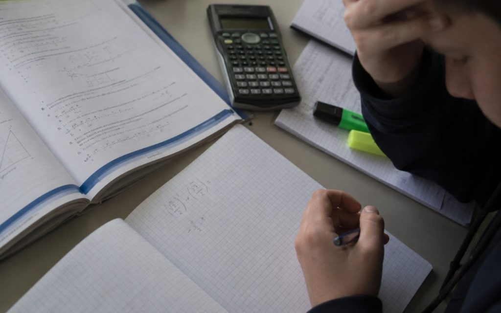 Zbliżenie na zeszyt z niedokończonymi obliczeniami matematycznymi, kalkulator i podręcznik podczas momentu pustki w głowie.