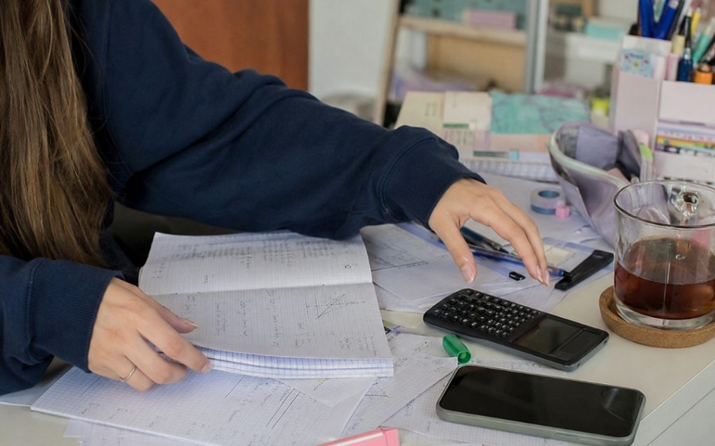 Przytulny kącik do nauki w sypialni z biurkiem, lampką i szkolnymi notatkami.