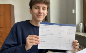 Uśmiechnięty nastolatek trzyma tablice matematyczne podczas nauki przy biurku.