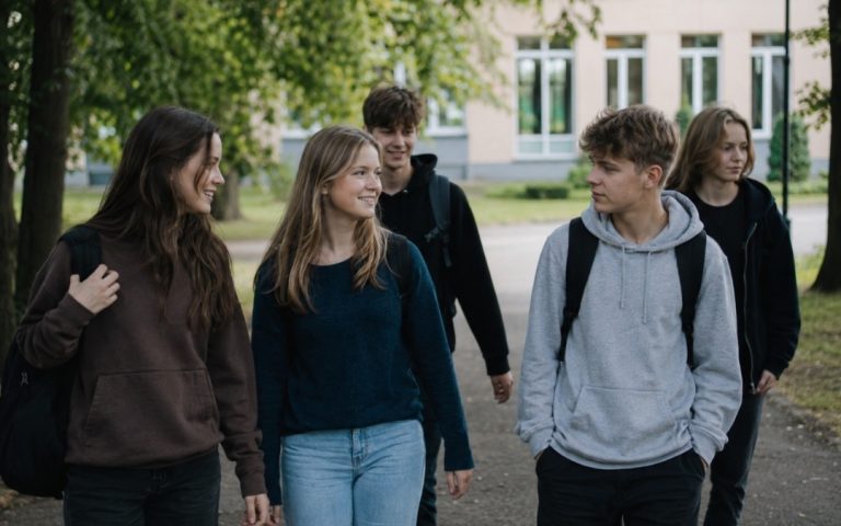 Grupa nastolatków z plecakami spaceruje po szkolnym parku po zajęciach.