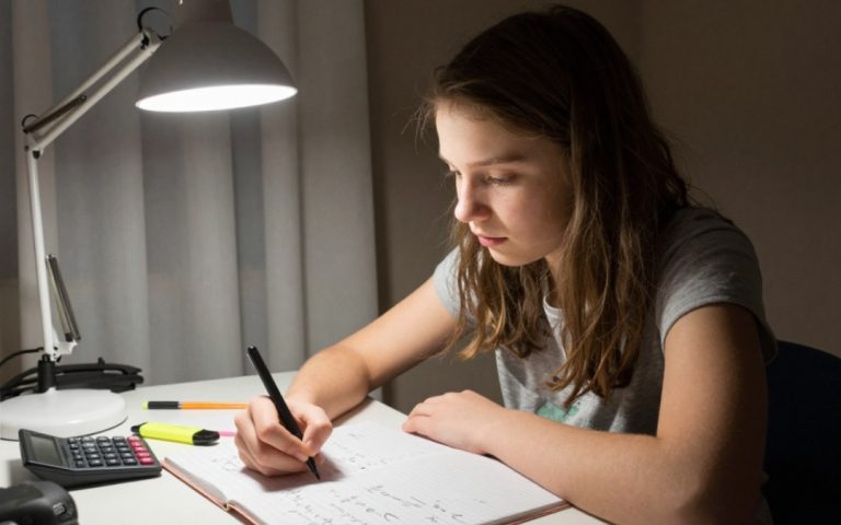 Nastolatka uczy się trygonometrii wieczorem przy biurku oświetlonym lampką.