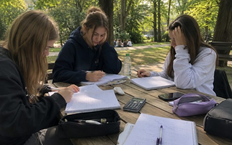 Trzy nastolatki uczą się razem matematyki w parku przy stoliku.