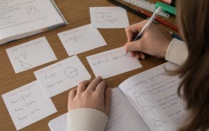 Skupiona uczennica uczy się matematyki w przytulnym pokoju, korzystając z notatek i materiałów pomocniczych.