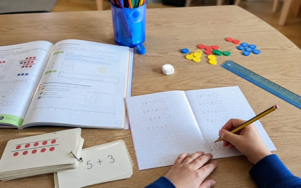 Chłopiec siedzi przy biurku i rozwiązuje zadania z matematyki w zeszycie.