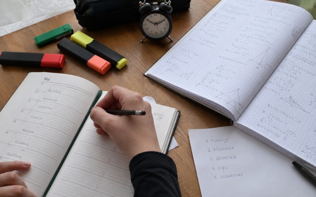 Licealista rozwiązuje zadania z matematyki przy biurku, korzystając z minutnika do planowania czasu nauki.