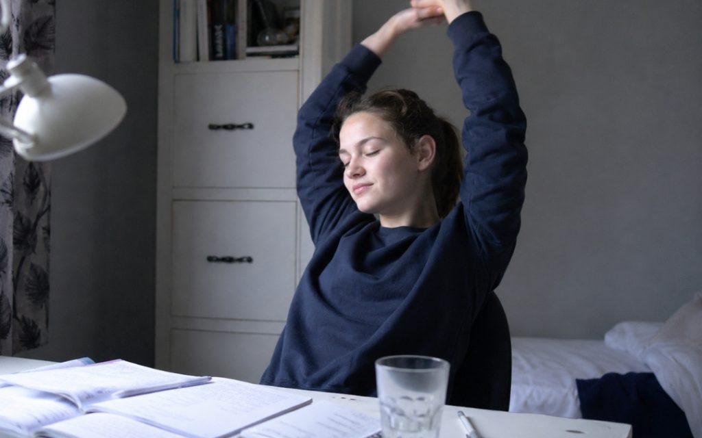 Licealistka robi krótką przerwę od nauki matematyki i rozciąga się przy biurku.