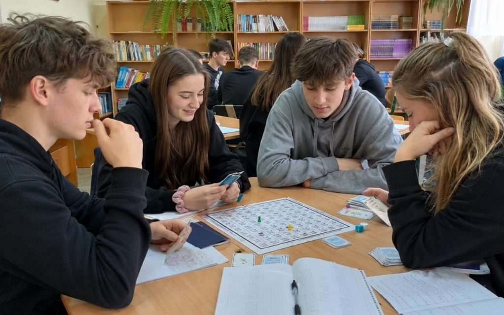 Uśmiechnięta grupa grająca we wspólną edukacyjną grę planszową.