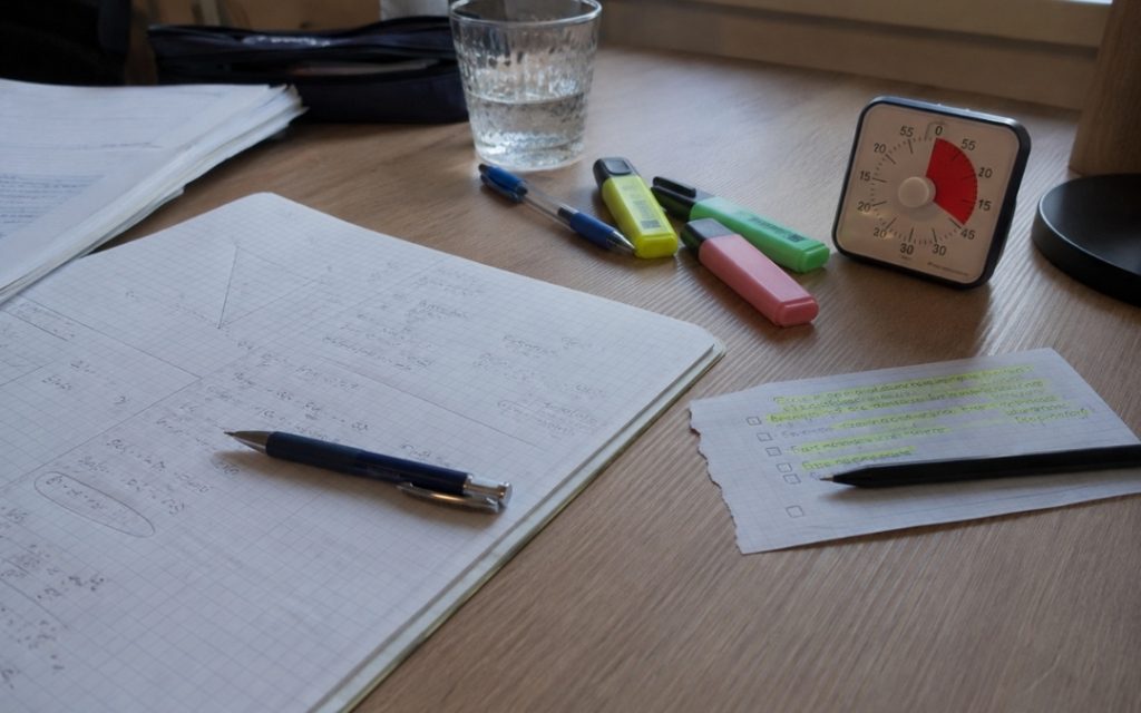 Zbliżenie na biurko z notatkami matematycznymi, zakreślaczami i minutnikiem odmierzającym czas nauki.