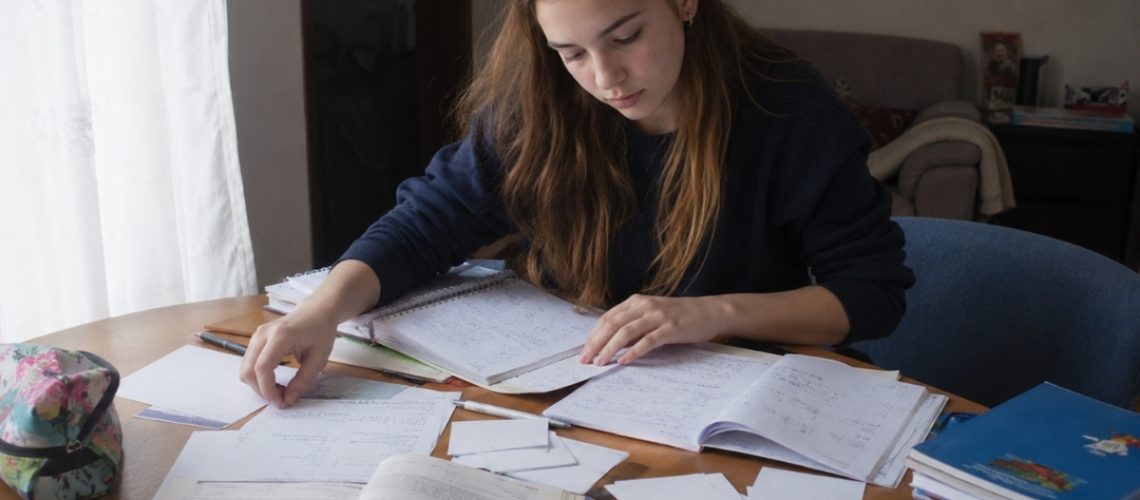 Nastolatka porządkuje materiały do sprawdzianu z matematyki na stole pełnym notatek i podręczników.