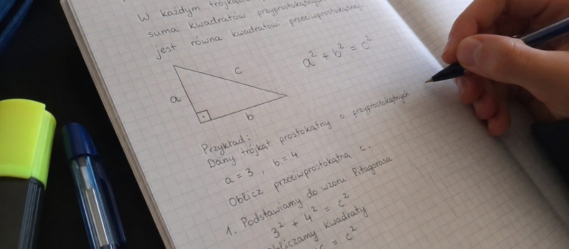 Zbliżenie na zeszyt z uproszczonym wyjaśnieniem twierdzenia Pitagorasa, rysunkiem trójkąta i obliczeniami.